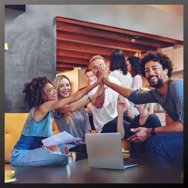 A diverse group of entrepreneurs sitting around a table and cheering each other on while collaborating together. 